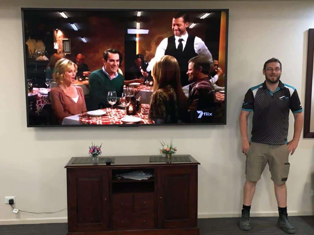 wall mounted tv above wooden entertainment unit with Installer standing next to tv