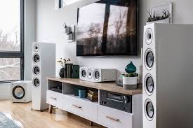White floor speakers beside an entertainment unit with another speaker, there is a wall mounted tv above the unit.